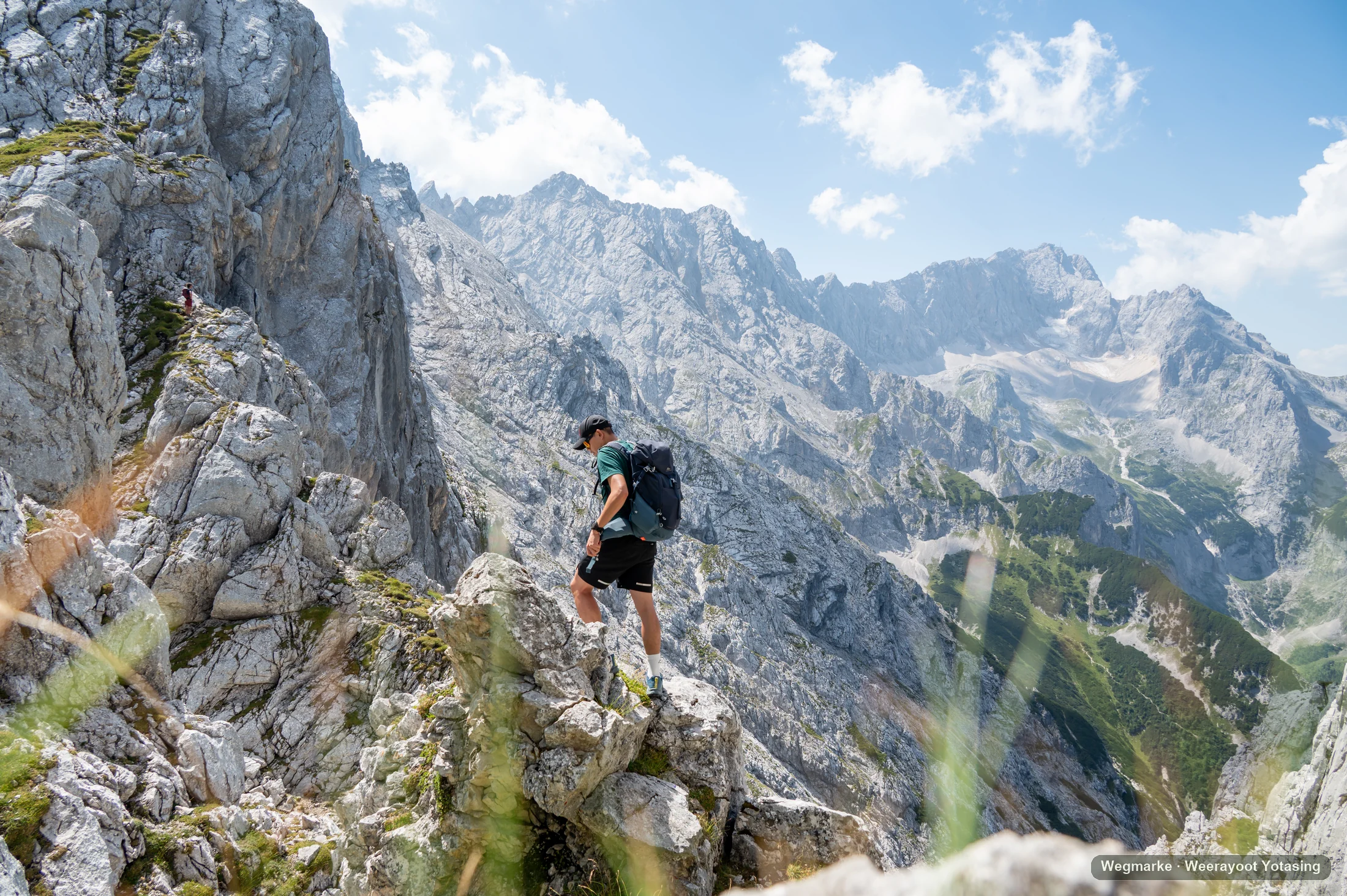 A hiker crosses a high rocky ridge above an alpine valley