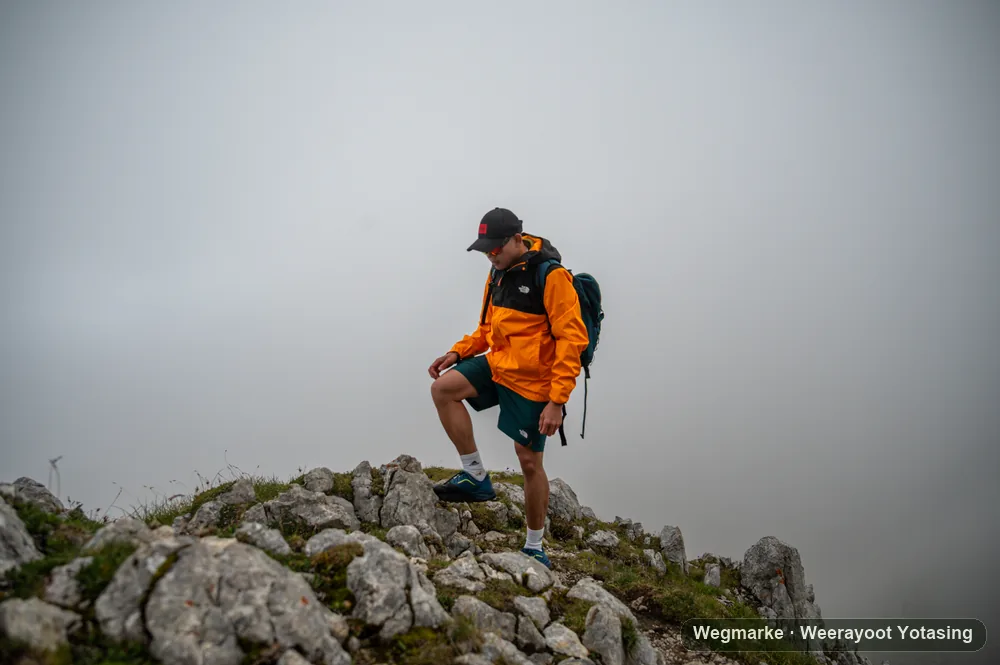 A hiker stepping through cloud on a rocky summit