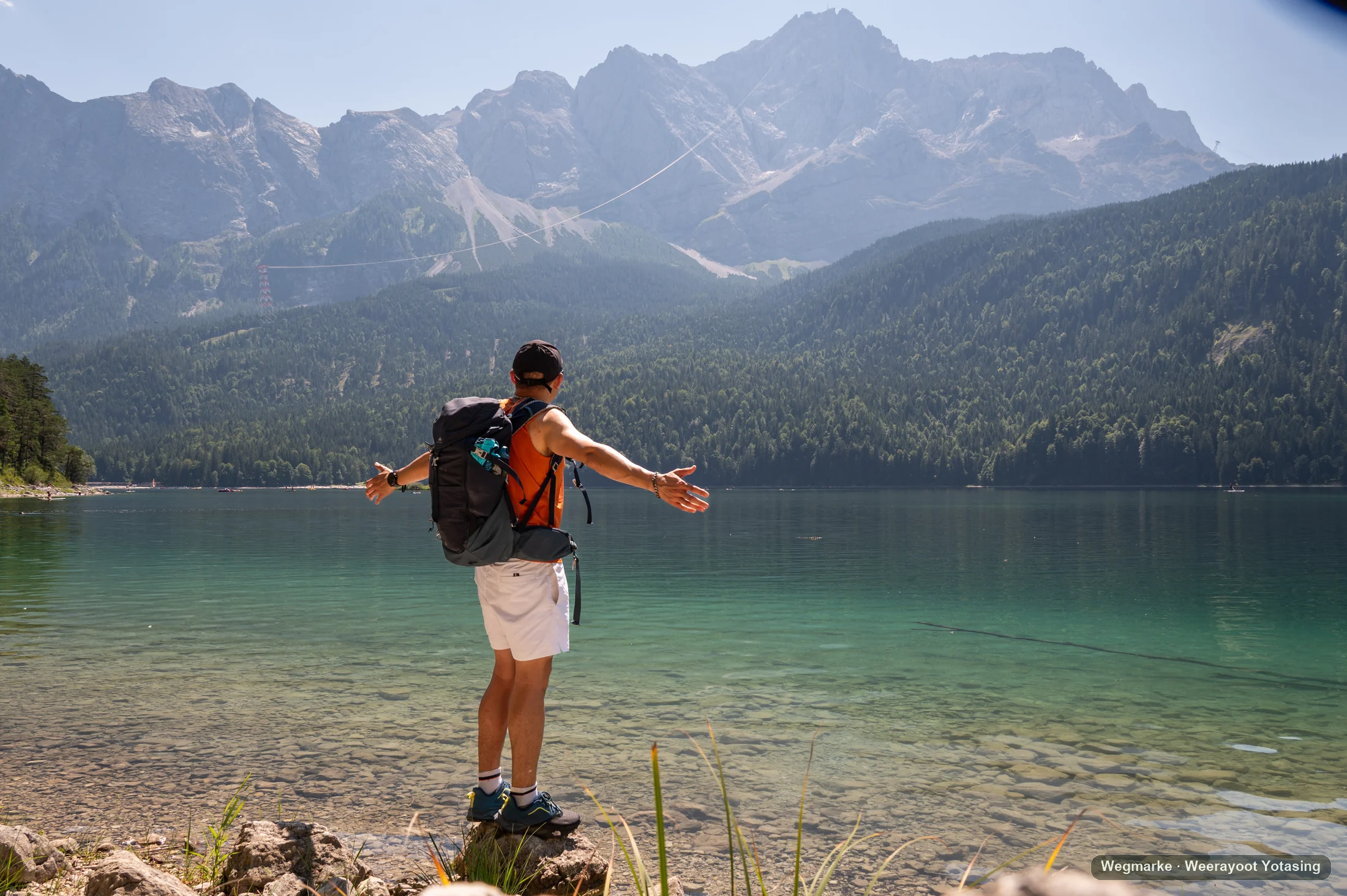 A hiker pauses with open arms beside a clear alpine lake